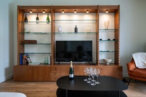 A living room with a wooden entertainment unit, a flat-screen TV, a black coffee table with a bottle and glasses, and a red sofa. - By the canal - Pets allowed - 3 bedrooms and an enclosed garden (Aÿ-Champagne)