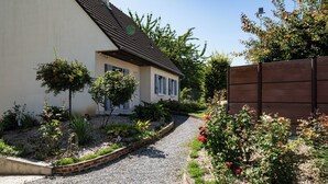 Une maison avec une allée en gravier, entourée d’un jardin où poussent différentes plantes et fleurs.