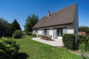 A two-story house with a tiled roof, a patio with a table and chairs, and a well-maintained lawn.
