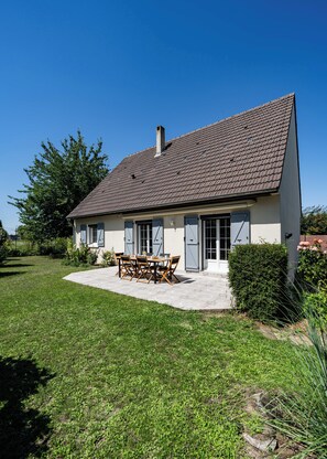 A two-story house with a tiled roof, a patio with a table and chairs, and a well-maintained lawn.