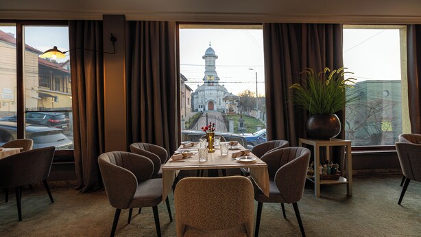 A dining area with a view of a church, a potted plant, and a table set for four. - Hotel Brilliant Plaza (Zalău)