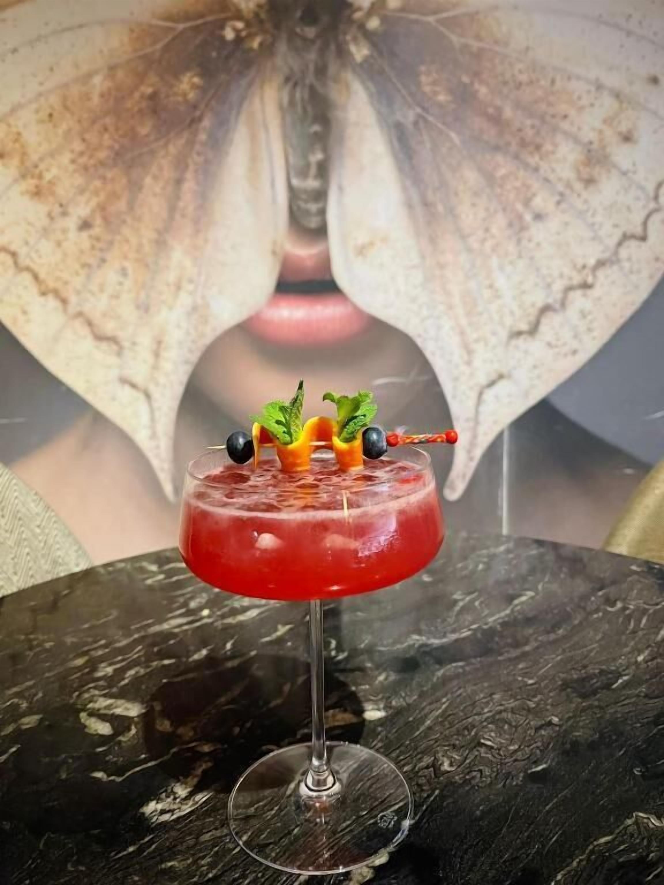 A cocktail with a garnish on a glass, placed on a table with a marble-like surface.