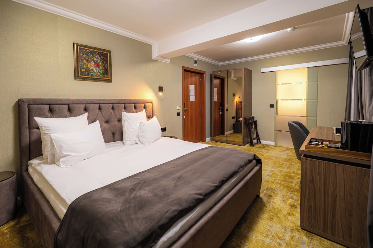 A hotel room with a large bed, a desk, a chair, a mirror, and a door.