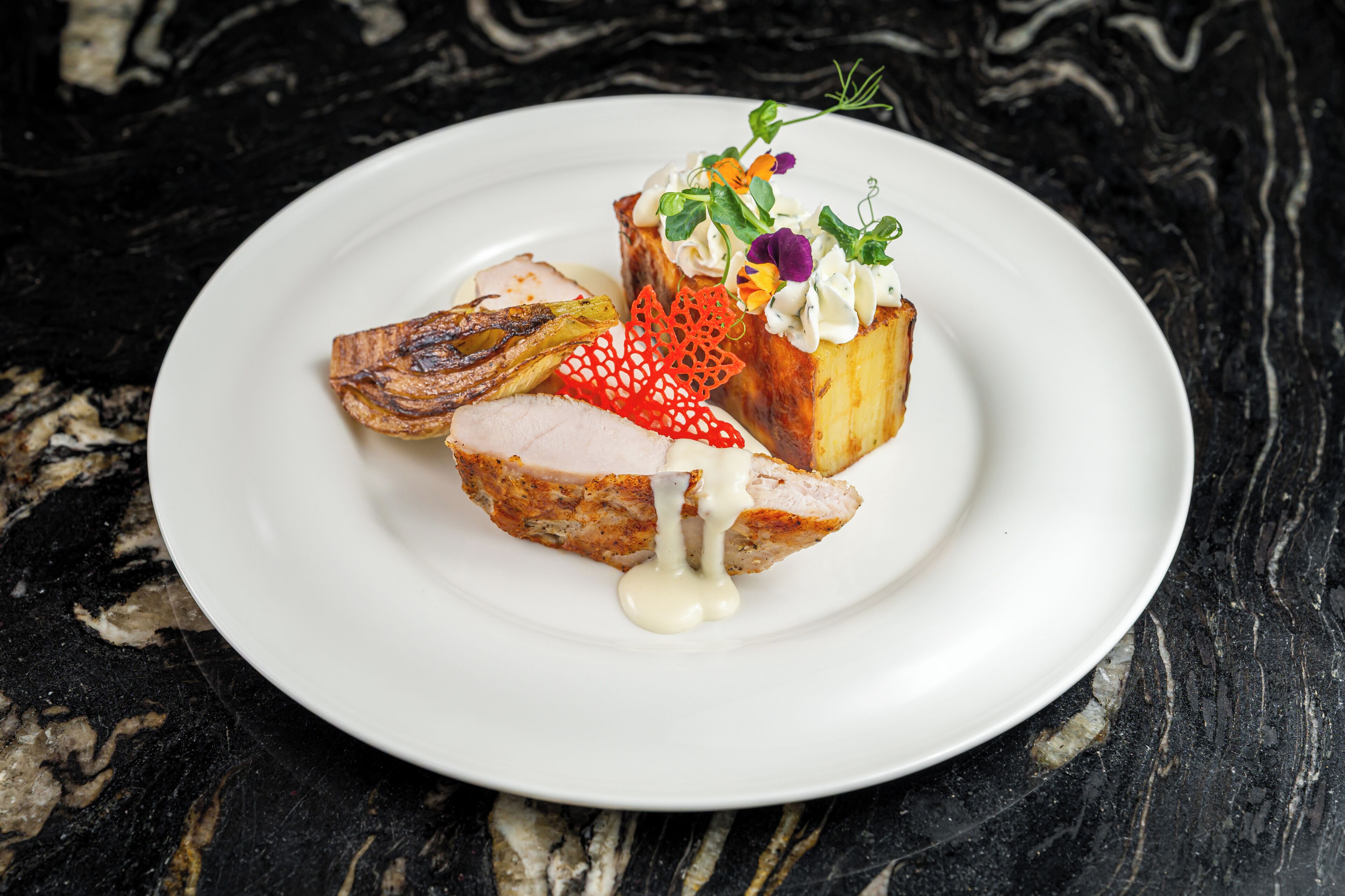 Une assiette blanche sur laquelle on voit un morceau de viande, un morceau de pain et un objet décoratif, le tout posé sur une surface en marbre foncé.