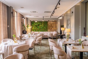 Et hotelspisested med flere borde og stole, en grøn væg med planter og et moderne loftdesign.