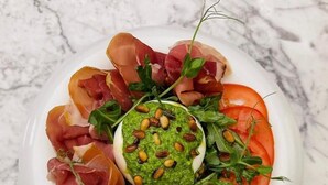 A bowl of food with prosciutto, arugula, tomatoes, and a green sauce with nuts. - Hotel Brilliant Plaza (Zalău)