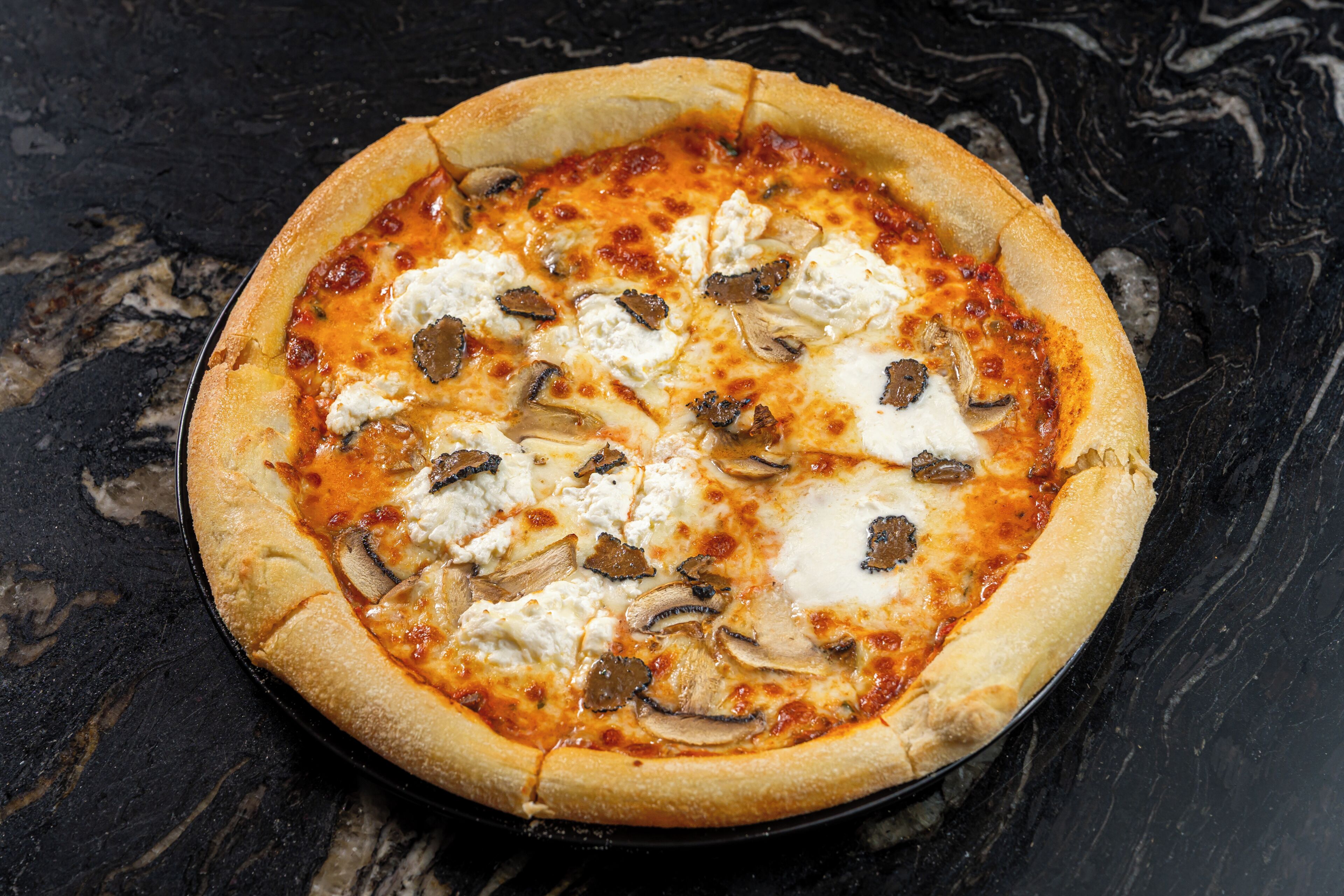 Una pizza con queso y champiñones sobre una superficie negra.