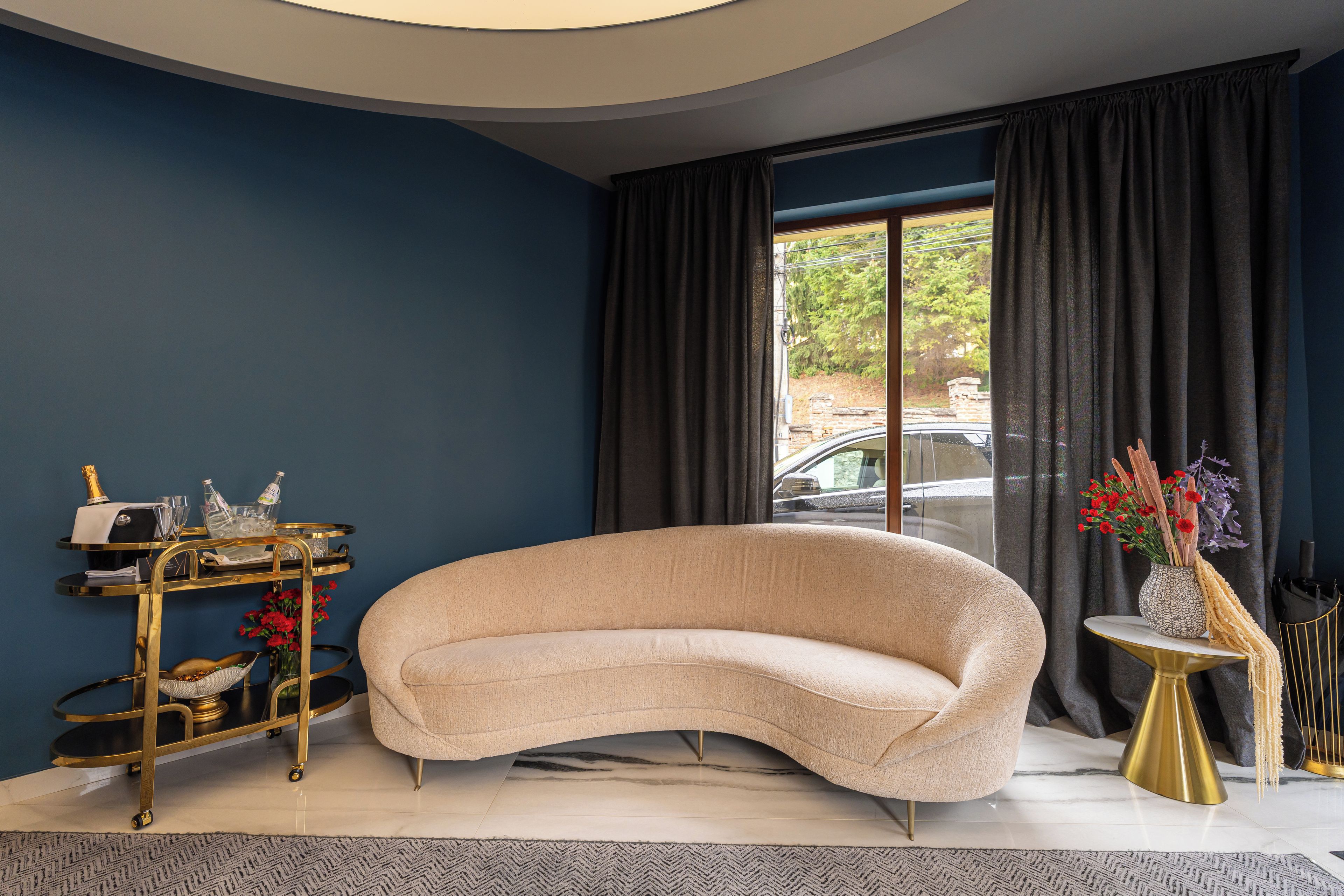 A modern living room with a curved sofa, a gold-framed side table, and a decorative vase with flowers.