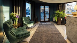 A hotel lobby with a curved ceiling, two green armchairs, a marble reception desk, a large potted plant, and a view of the street through the entrance doors. - Hotel Brilliant Plaza (Zalău)