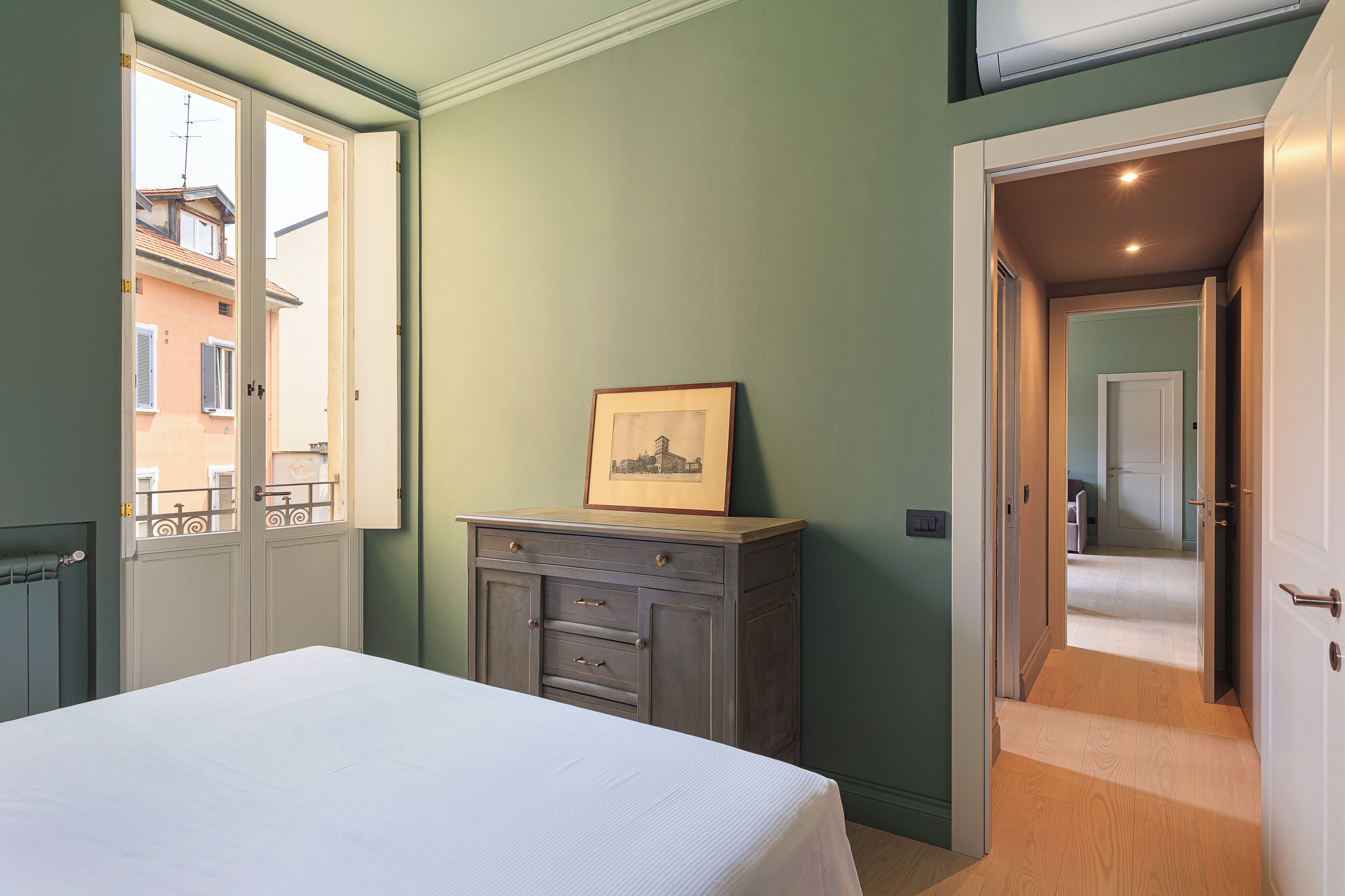 A bedroom with a bed, a dresser, and a door leading to another room.