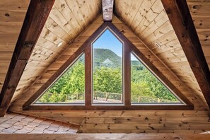 A triangular wooden ceiling with a view of a forested hill.