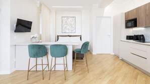Una cocina moderna con encimera blanca, taburetes de bar color turquesa y un televisor de pantalla plana montado en la pared.
