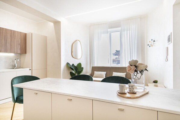 Una cocina moderna con encimera de mármol, sillas verdes y una zona de comedor con mesa blanca.