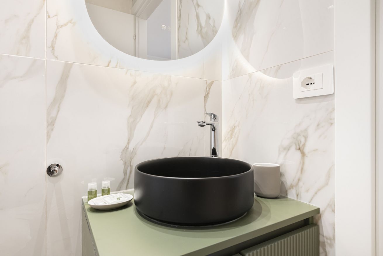 Un baño con un lavabo redondo, un espejo y un inodoro.