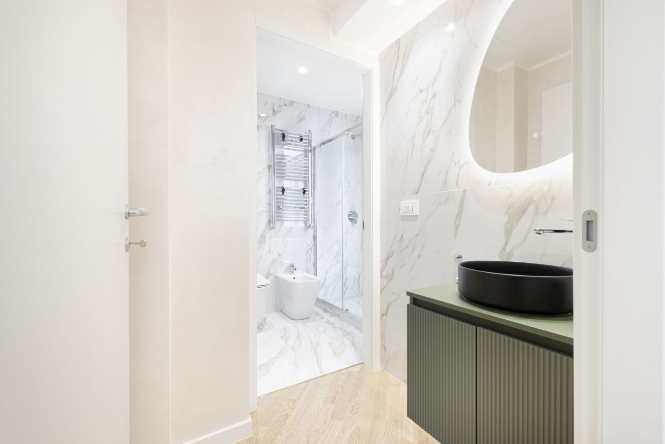 A modern bathroom with a marble shower, a freestanding bathtub, and a large mirror.