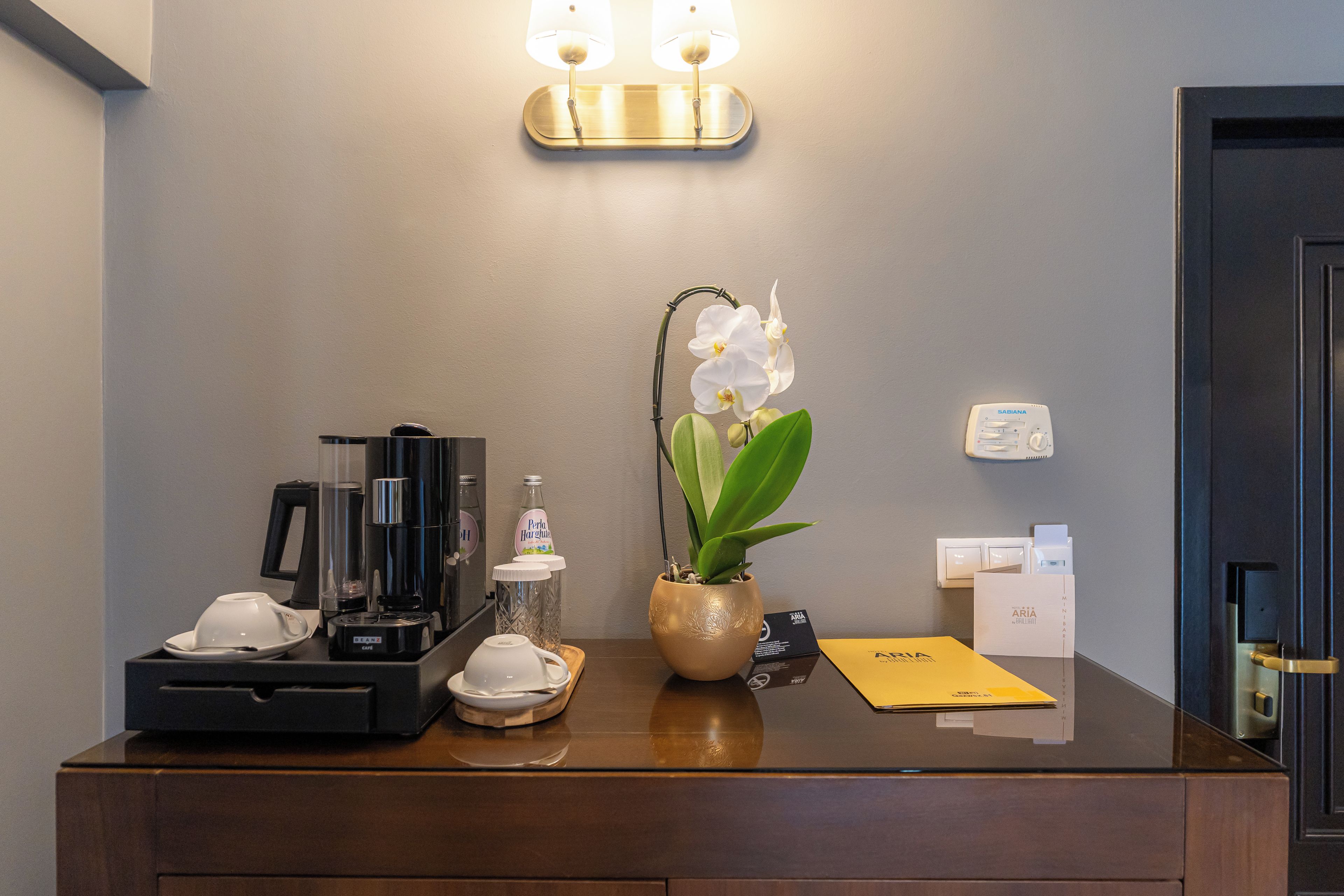 A hotel reception desk with a coffee machine, a potted orchid, and a Sabiana thermostat.