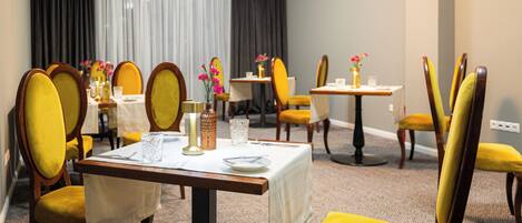Un comedor de hotel con sillas tapizadas en amarillo, manteles blancos y centros de mesa florales.