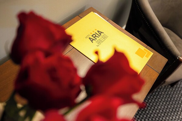 A yellow envelope with "HOTEL ARIA" and "by Pullman" text, placed on a wooden surface with red flowers in the foreground.