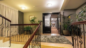 A staircase with a wooden handrail and metal balusters, leading to a landing with a rug and potted plants. - Aria by Brilliant (Zalău)