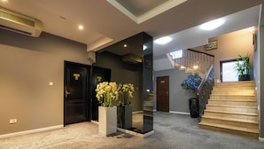 A hallway with carpeted flooring, a staircase with a railing, and a potted plant. - Aria by Brilliant (Zalău)