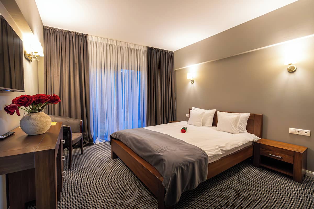 Una camera d'albergo con un letto, un comodino, una lampada e una scrivania con un vaso di fiori.