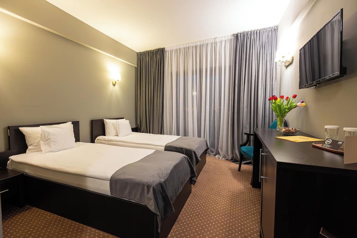 Camera d'albergo con due letti, una scrivania, una sedia, una televisione e una finestra con tende.