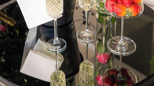 A table with a bottle of champagne, a glass of champagne, a glass of water, a glass of champagne with strawberries, and a vase with roses. - Aria by Brilliant (Zalău)