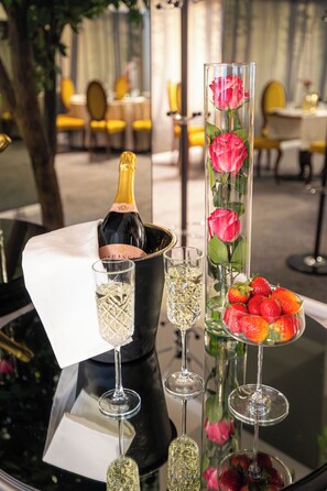 A table with a bottle of champagne, a glass of champagne, a glass of water, a glass of champagne with strawberries, and a vase with roses.