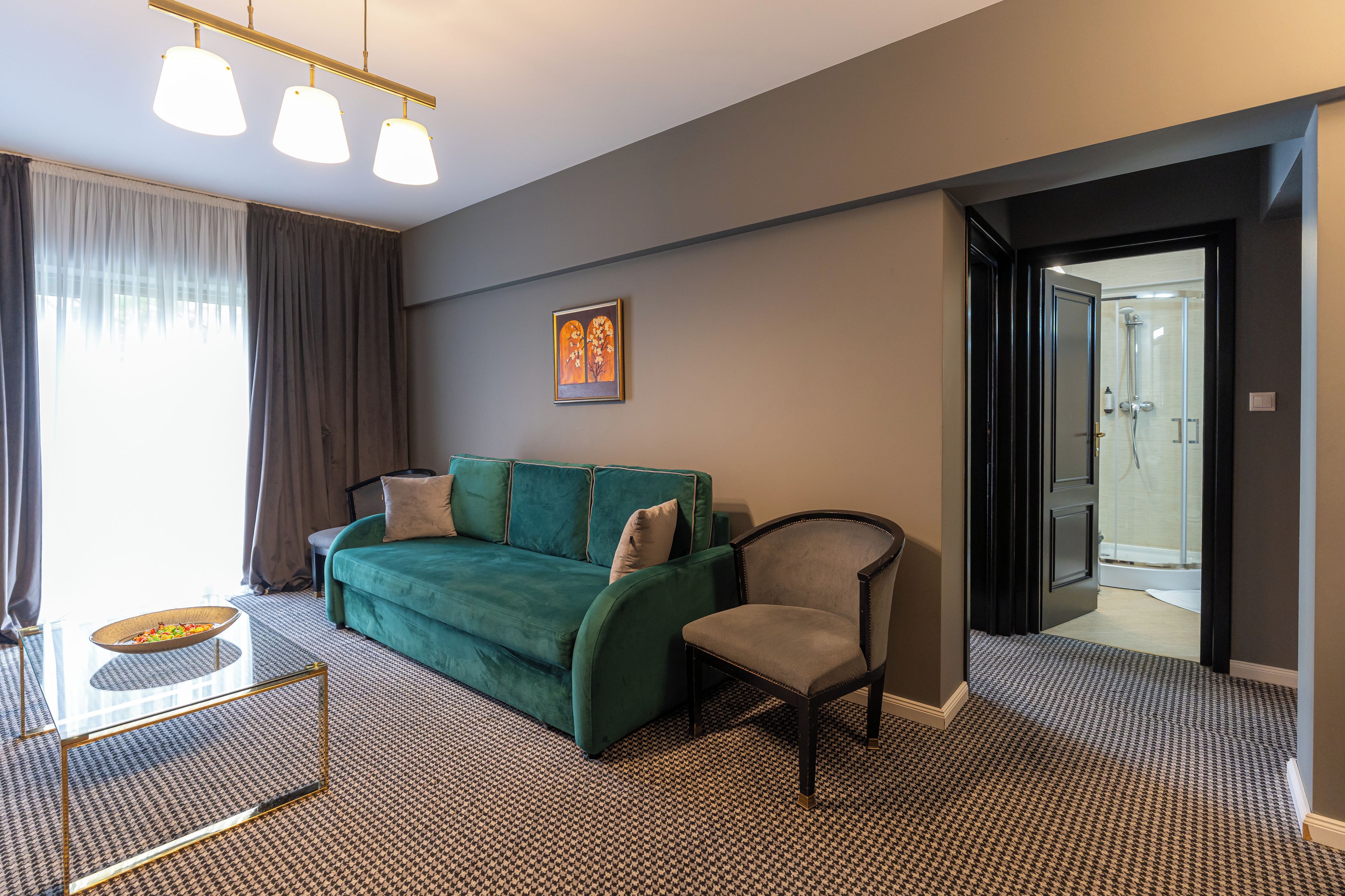 A modern hotel room with a green sofa, a chair, a small table, and a painting on the wall.
