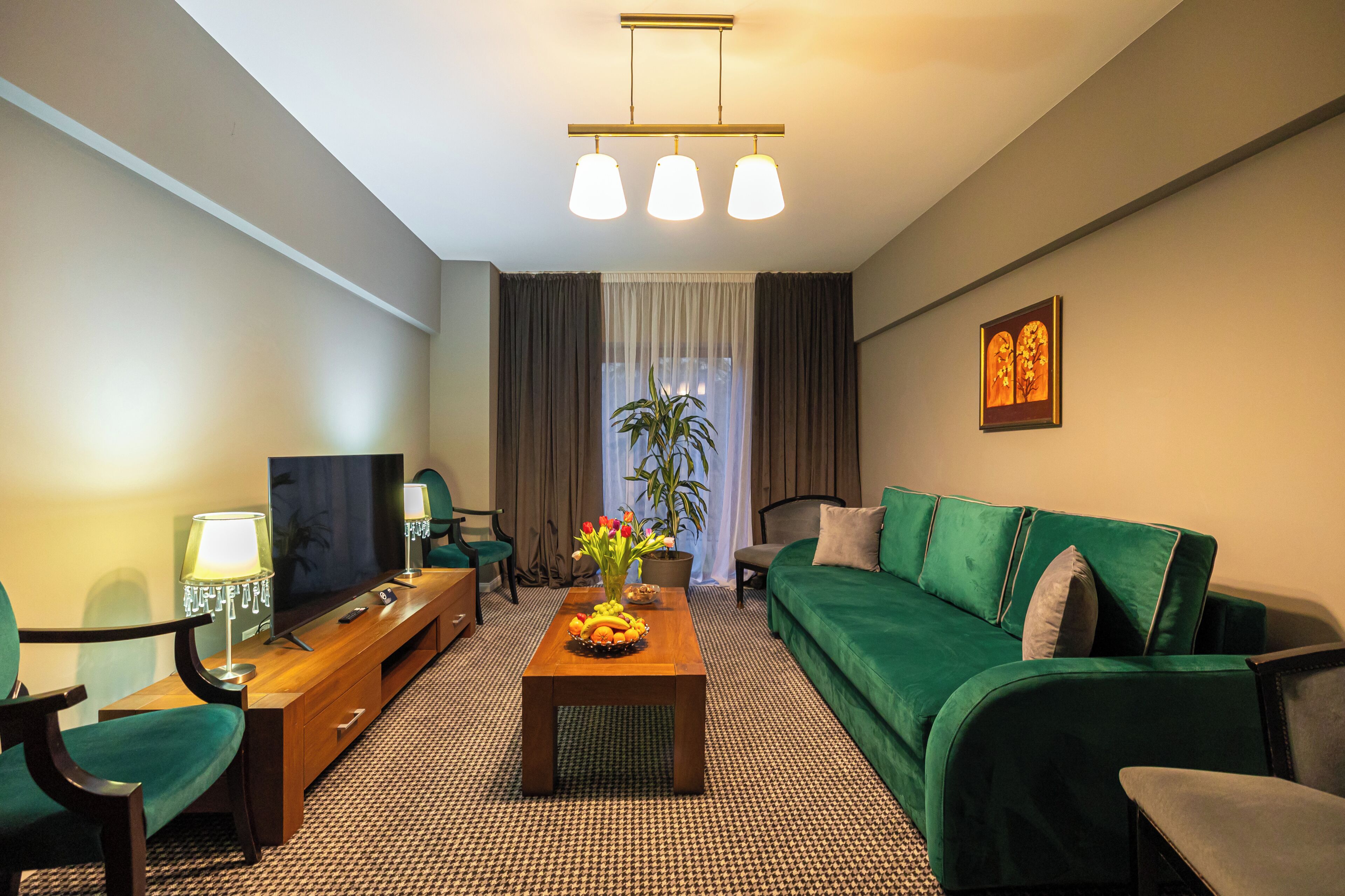 A hotel room with a green sofa, a wooden coffee table with fruit, a TV, and a plant.