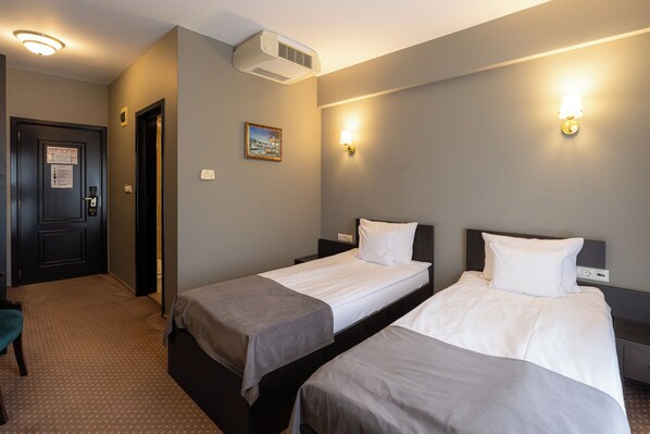 A hotel room with two single beds, a door with a lock, a wall-mounted air conditioner, and a painting.
