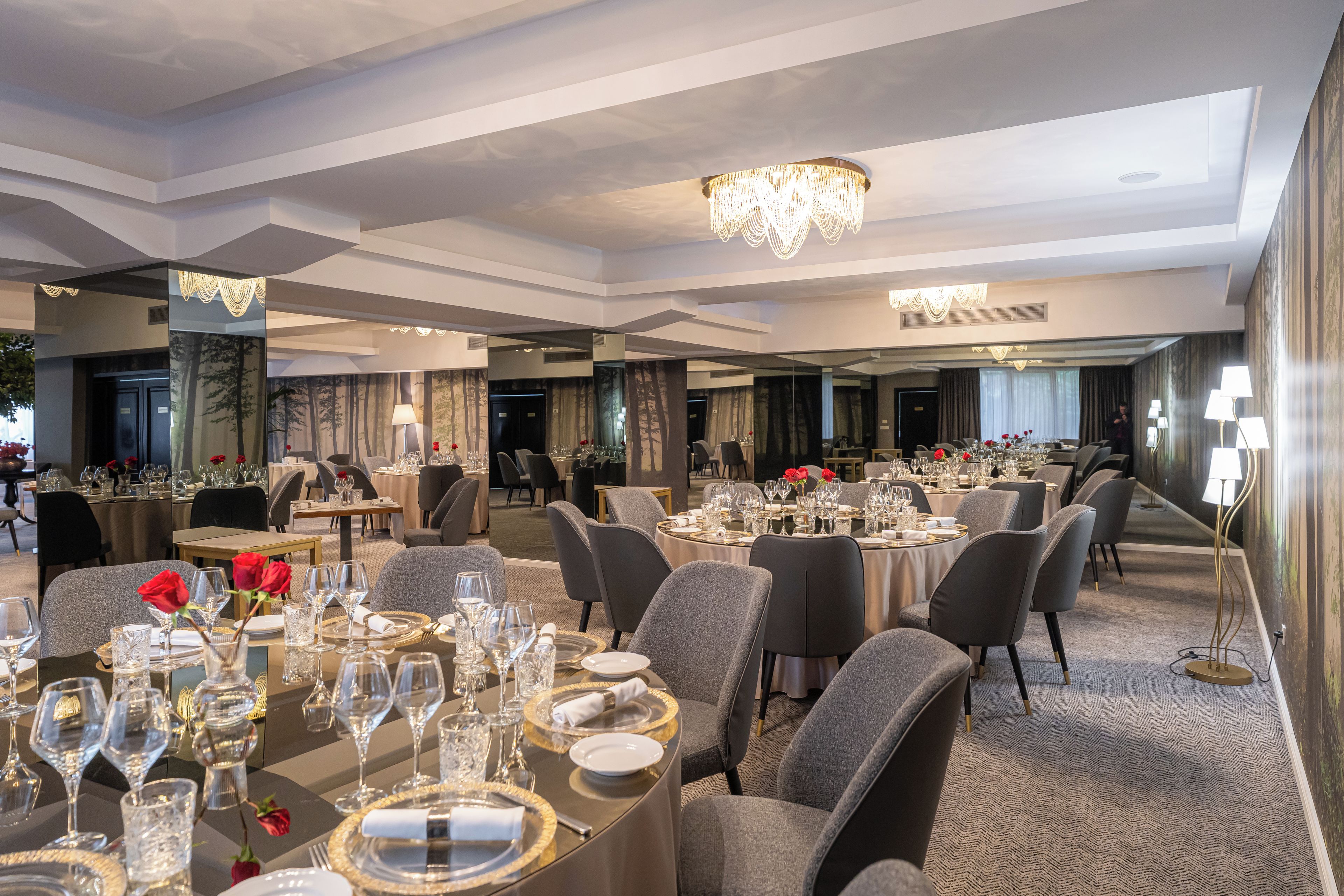 A hotel dining area with multiple tables set for guests, featuring a chandelier and modern decor.