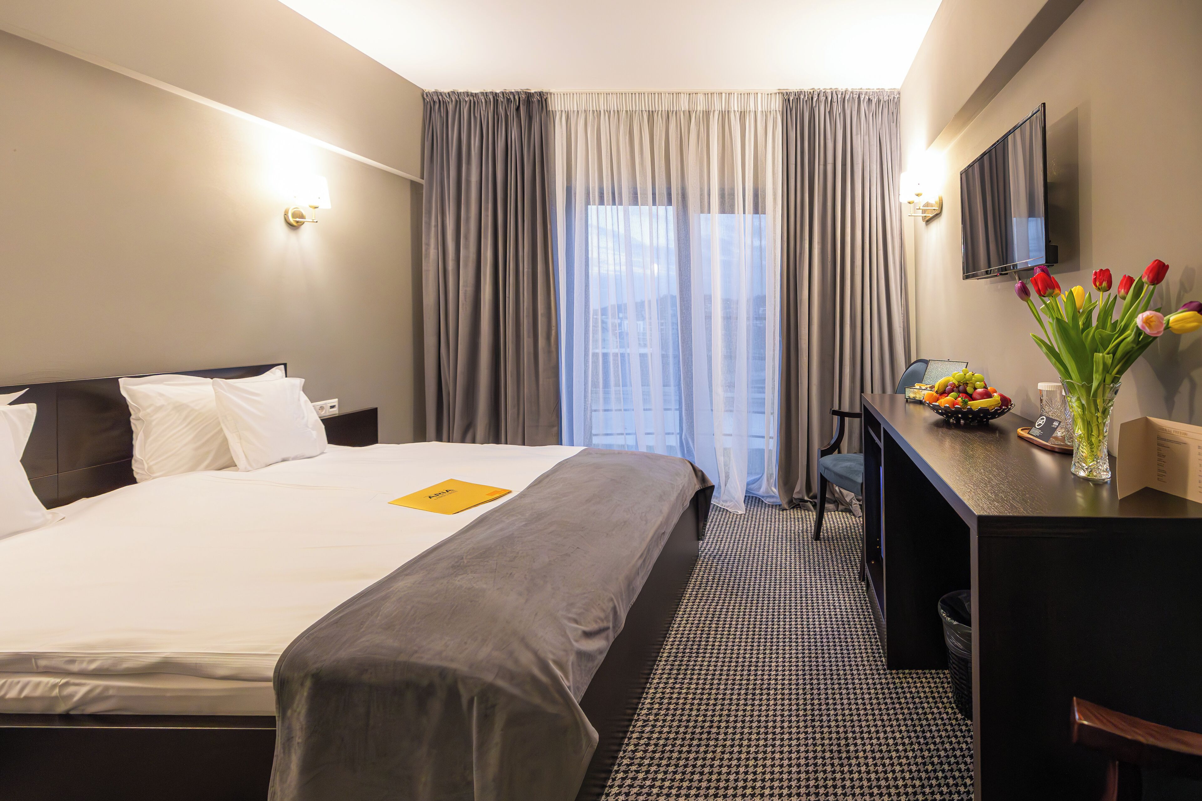 Een hotelkamer met een bed, een bureau, een stoel, een televisie en een raam met gordijnen.