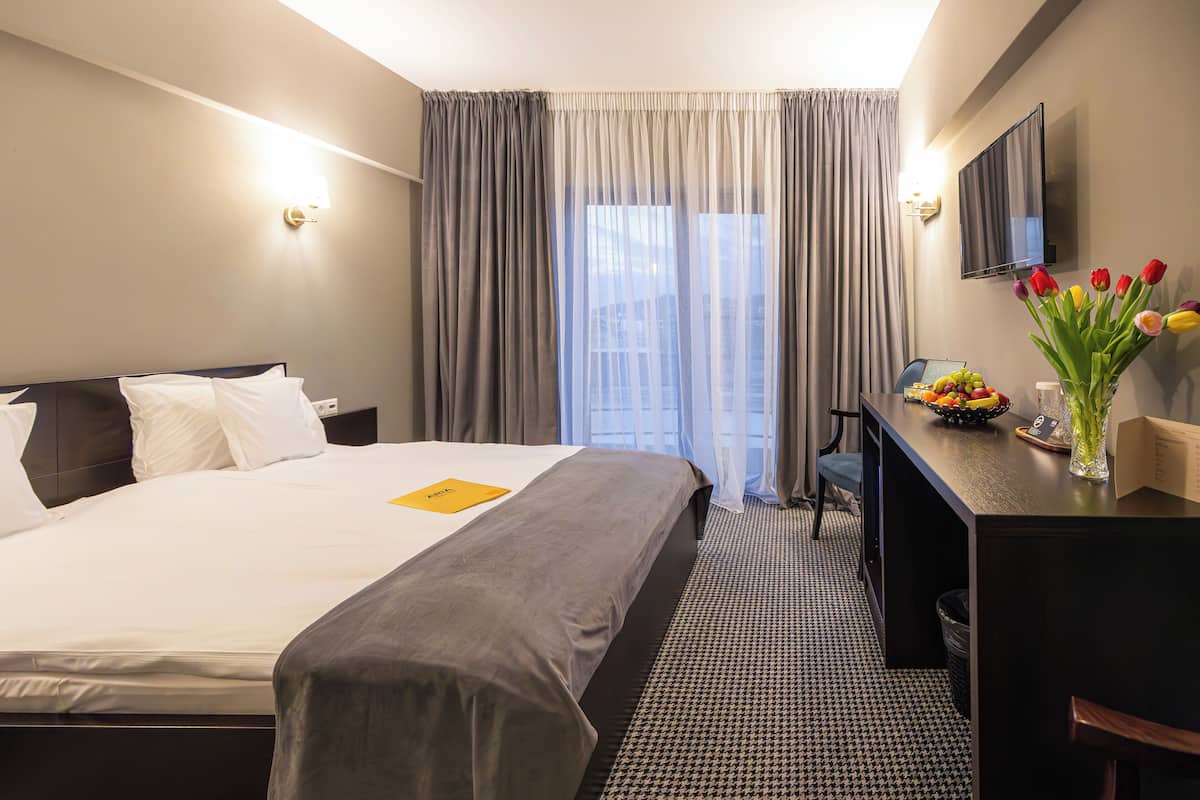 Hotellihuone, jossa on sänky, työpöytä, tuoli, televisio ja ikkuna, jossa on verhot.