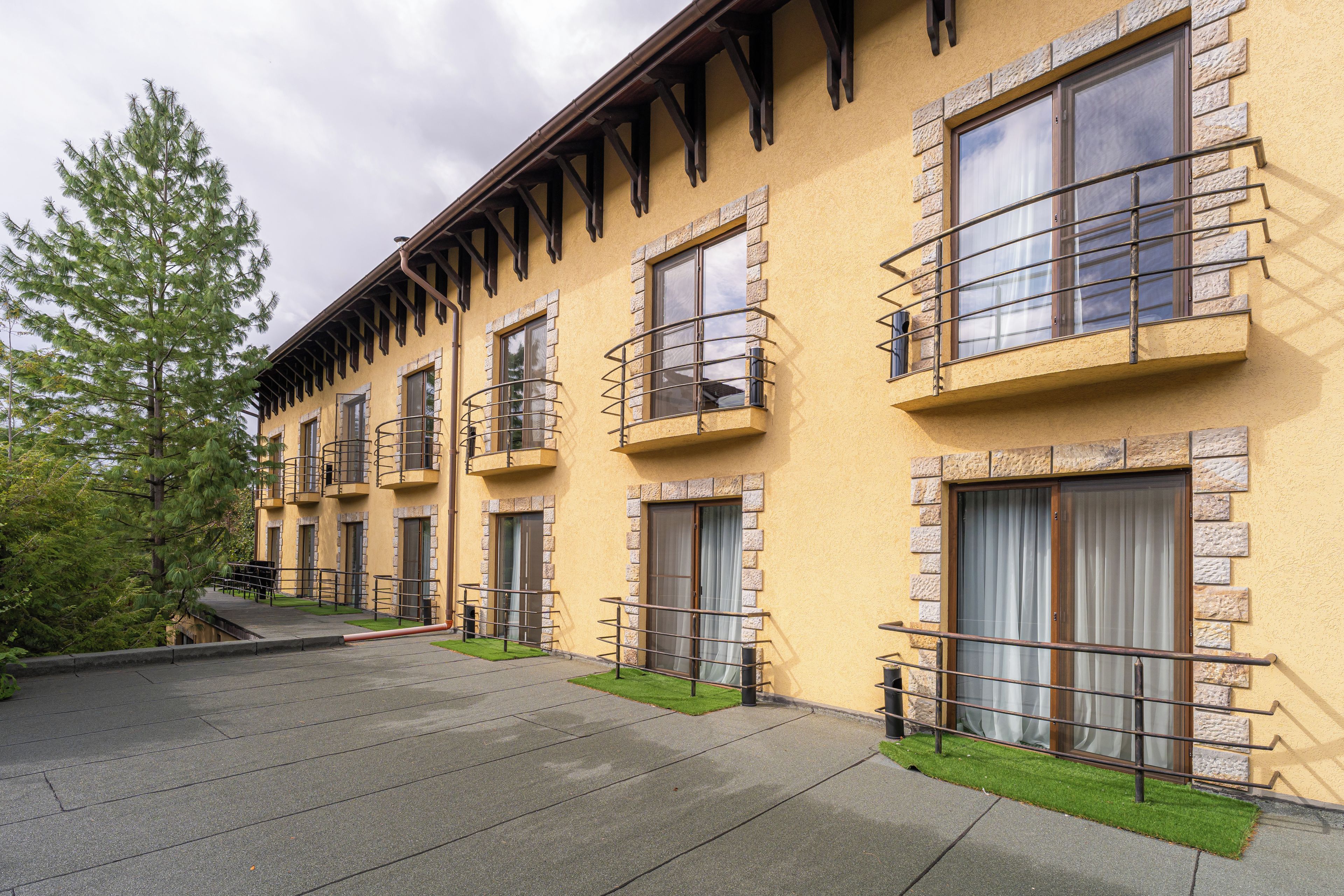 A multi-story building with balconies, a paved driveway, and a grassy area.