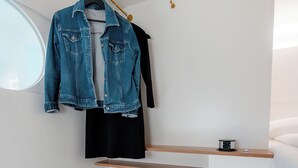 A compact, modern bathroom with a wooden vanity, a black suitcase, a denim jacket, and a black shirt hanging on a wooden rack. - Grand Pods  (Vienna)