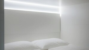 A modern bedroom with a large bed, white linens, and a headboard with integrated lighting. - Grand Pods  (Vienna)