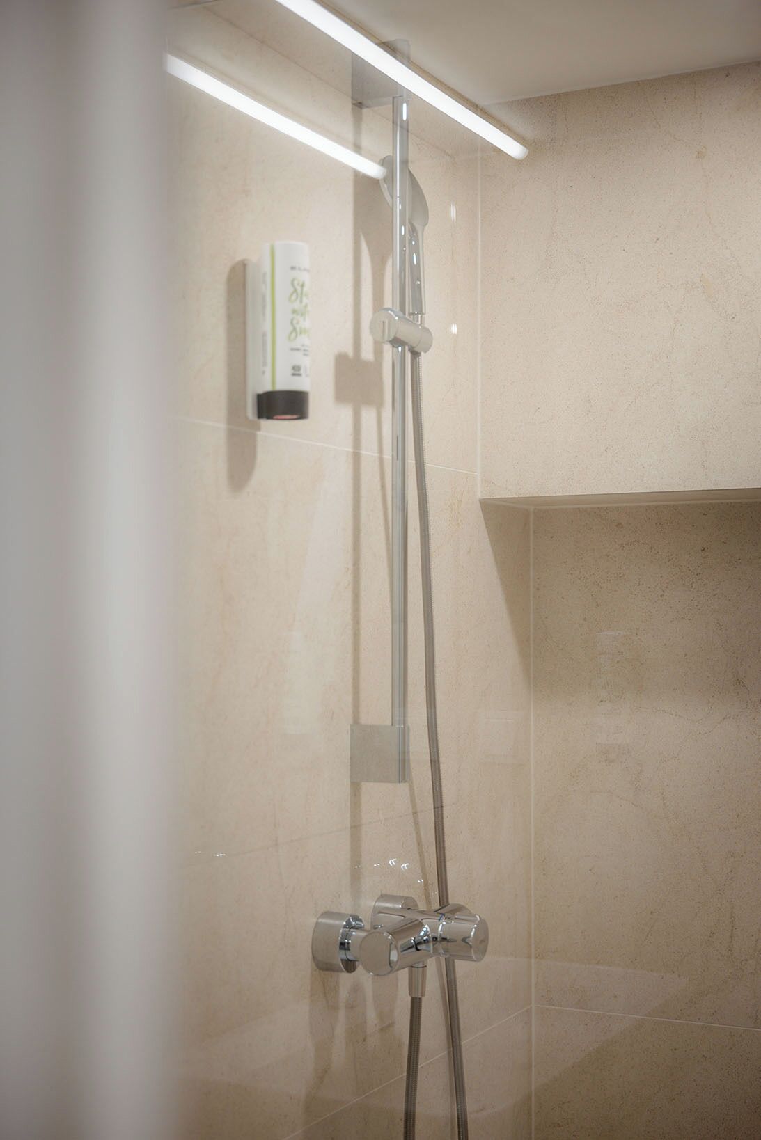 Une douche équipée d’un pommeau de douche à main, d’un panneau de commande mural et d’un espace de douche clos par des parois en verre.