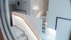 A modern interior with a staircase, a door with a checkmark sign, and a circular window frame. - Grand Pods  (Vienna)