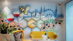 A room with a yellow sofa, a dining table with chairs, and a mural on the wall depicting a cityscape with a Ferris wheel. - Grand Pods  (Vienna)