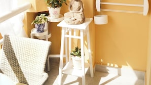Une pièce avec un mur jaune, une statue de Bouddha et plusieurs plantes en pot disposées sur une étagère blanche.
