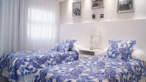 Une chambre avec deux lits, des murs blancs et une table de chevet avec une lampe.