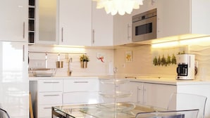 Une cuisine moderne avec des meubles blancs, un réfrigérateur en acier inoxydable, un four encastré et une machine à café.