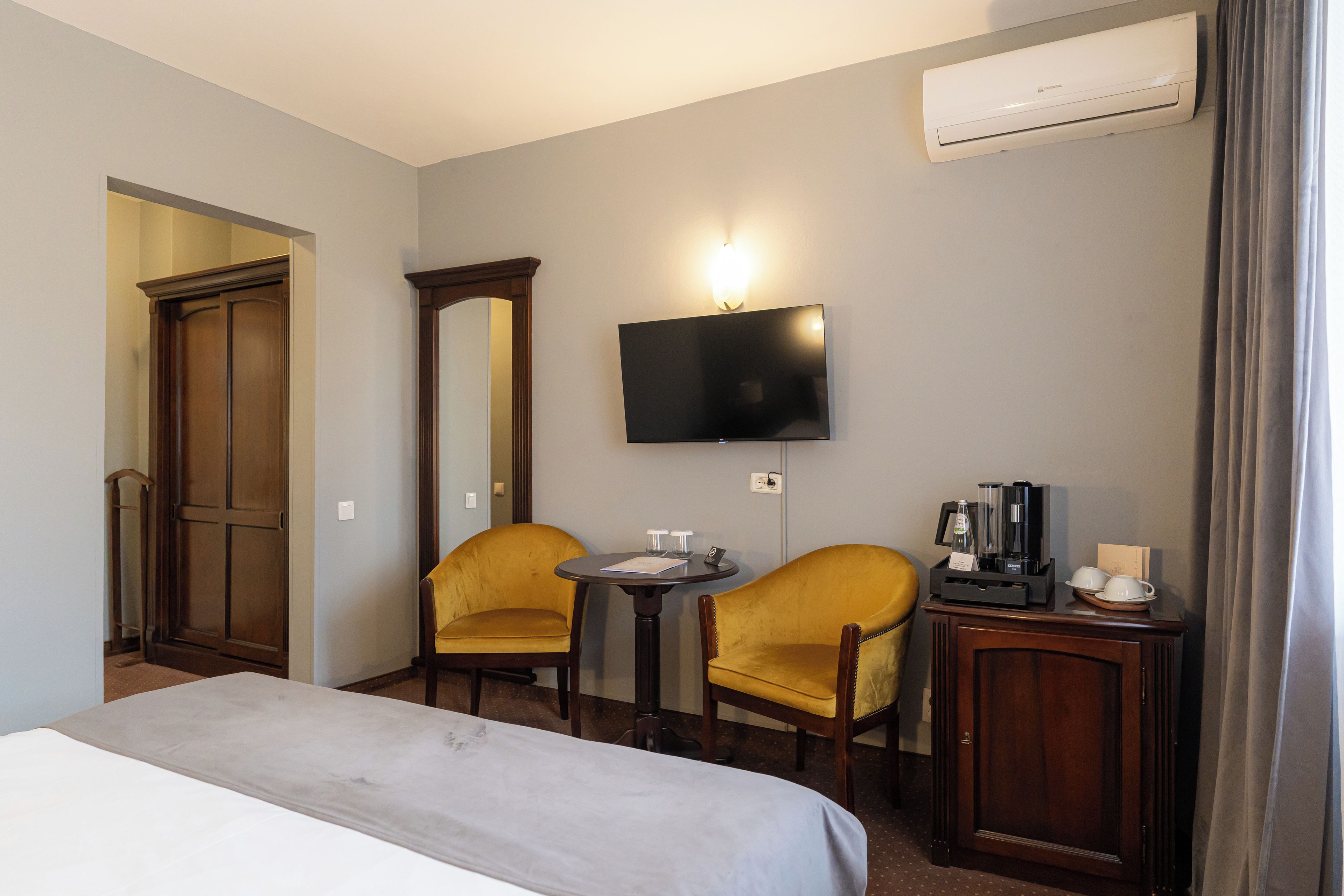 A hotel room with a bed, two chairs, a small table, a TV, and a coffee station.