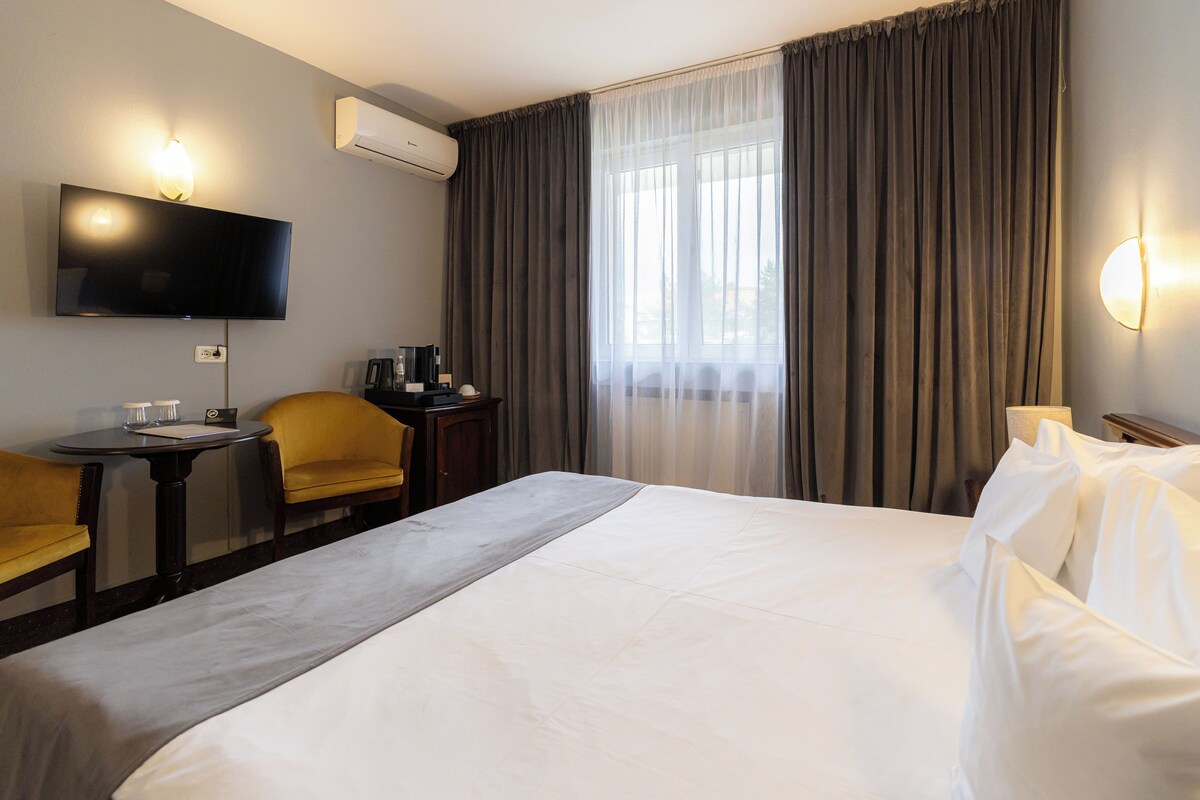 Une chambre d’hôtel avec un lit, un bureau, une chaise, une télévision et une fenêtre avec des rideaux.