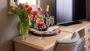 A hotel room with a large mirror, a flat-screen TV, a minibar, a desk with a vase of flowers, and a wall-mounted air conditioner.