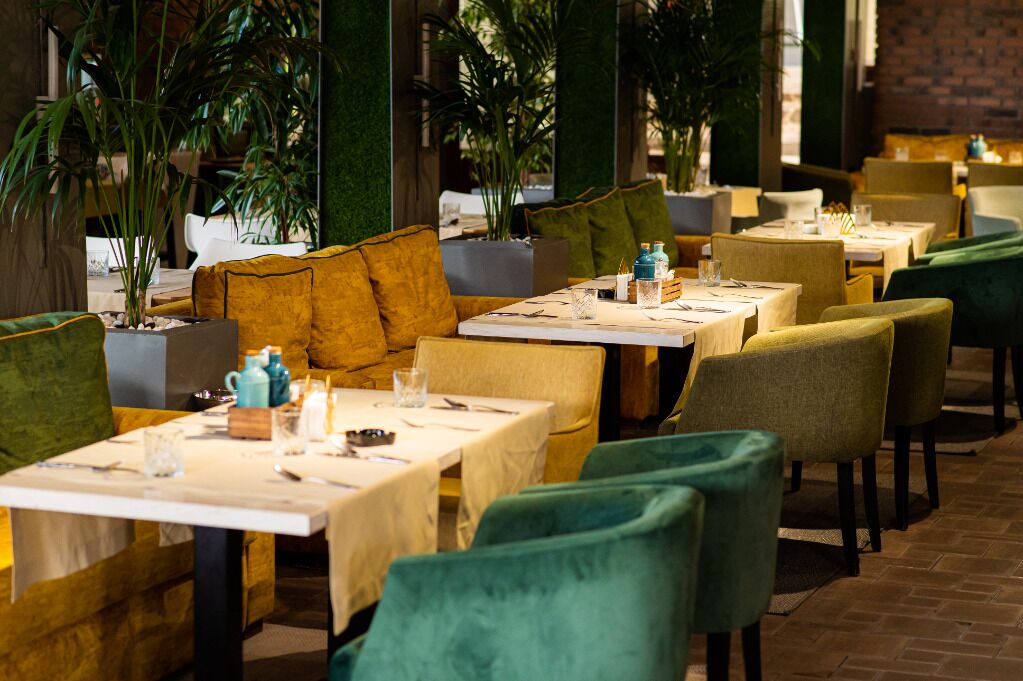 Restaurante com mesas montadas para refeições, assentos acolchoados e plantas em vasos.