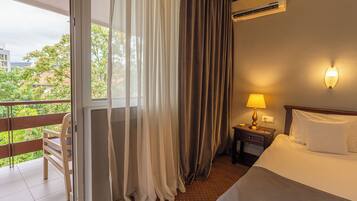 Habitación de hotel con cama, mesita de noche con lámpara, ventana con cortinas y equipo de aire acondicionado.