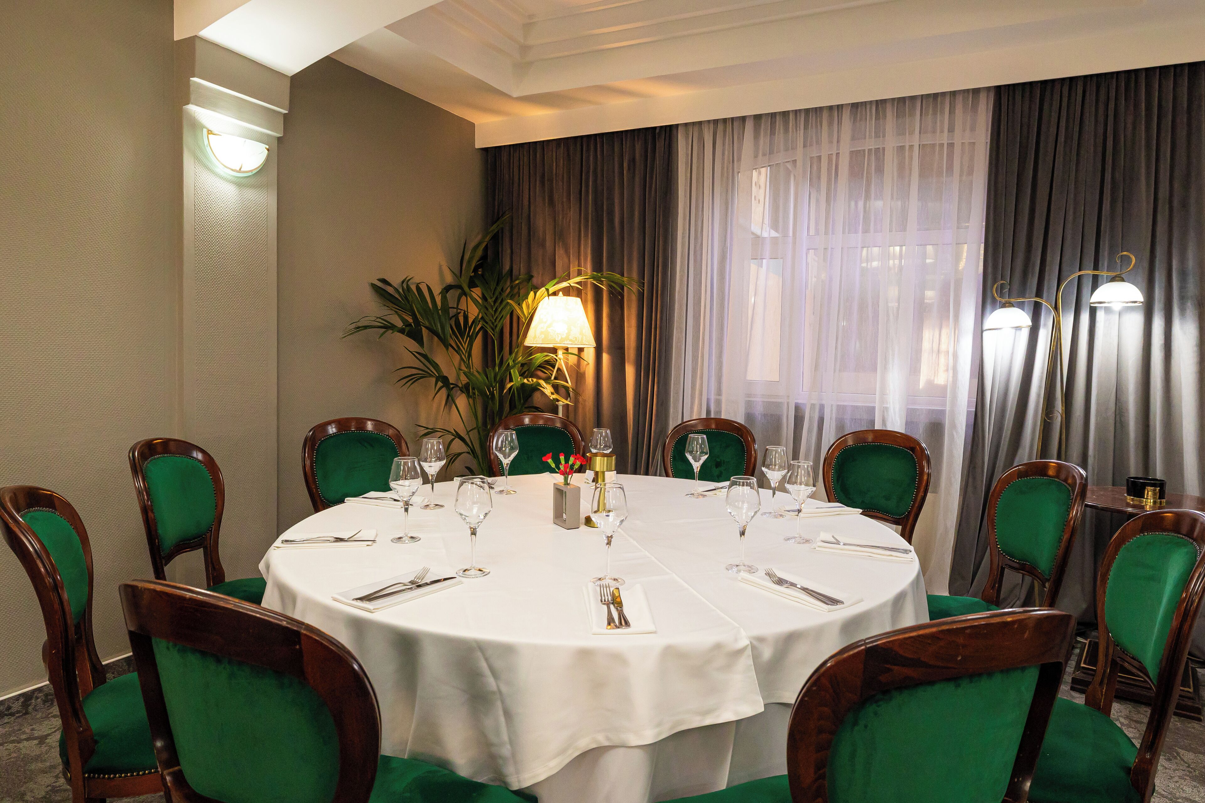A round dining table with a white tablecloth, surrounded by green upholstered chairs.