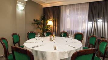 Una mesa de comedor redonda con mantel blanco, rodeada de sillas tapizadas en verde.